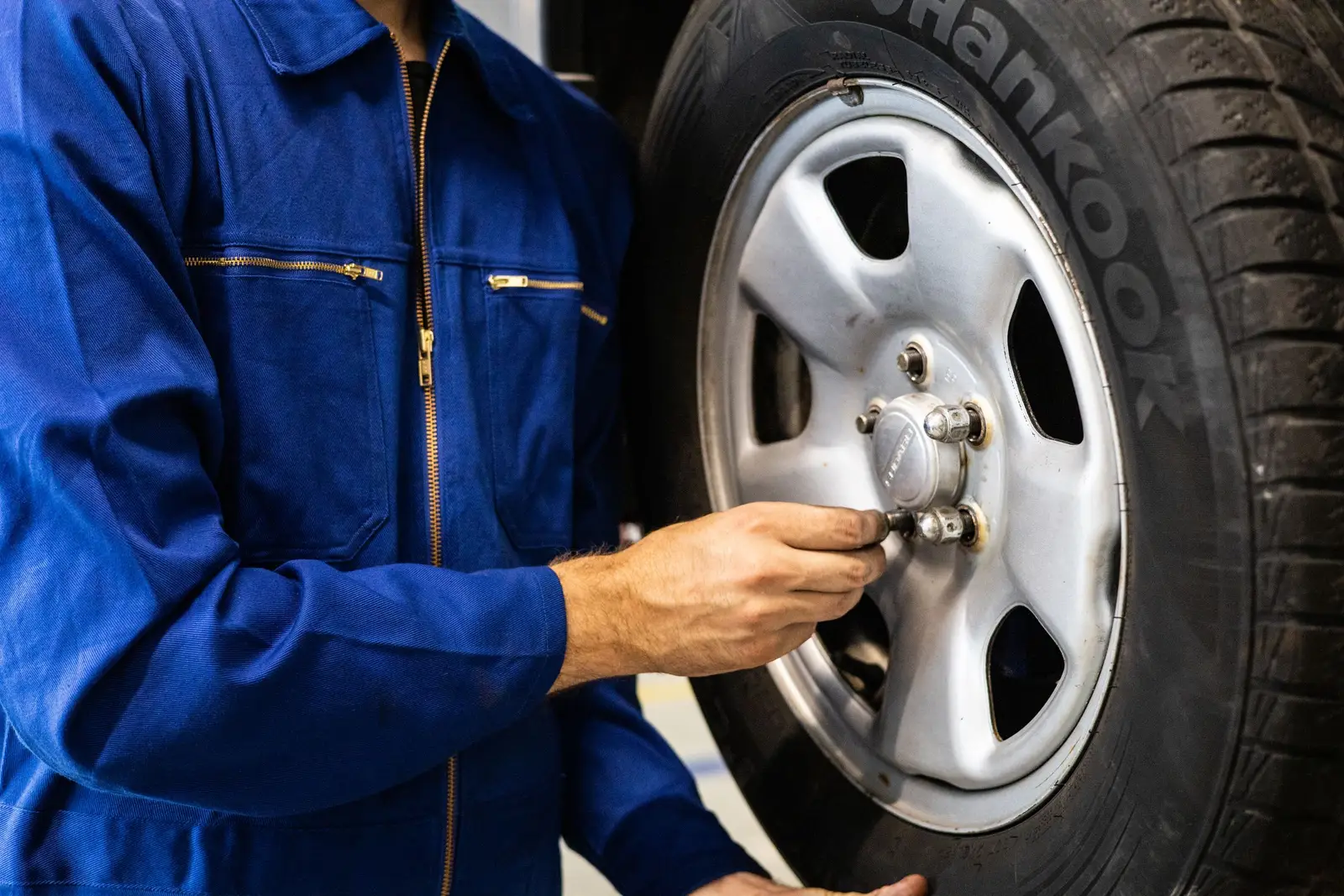 Mechanic in blue coveralls tightening lug nuts on a wheel
