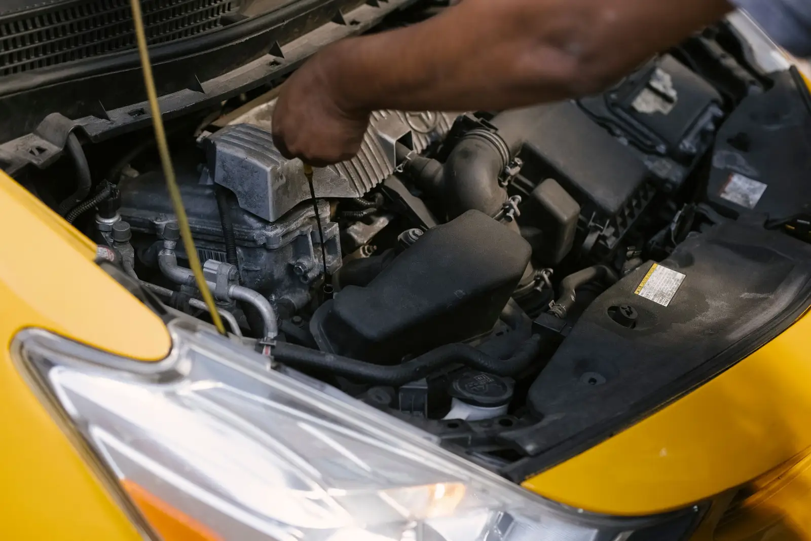 Hand checking the oil dipstick under the hood of a yellow car