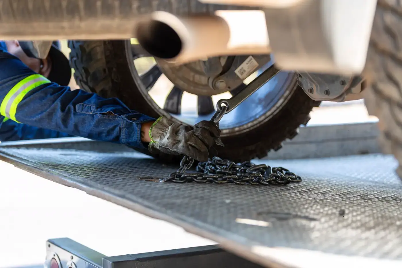 Gloved hand hooking a tie-down chain to a truck wheel on a flatbed tow deck