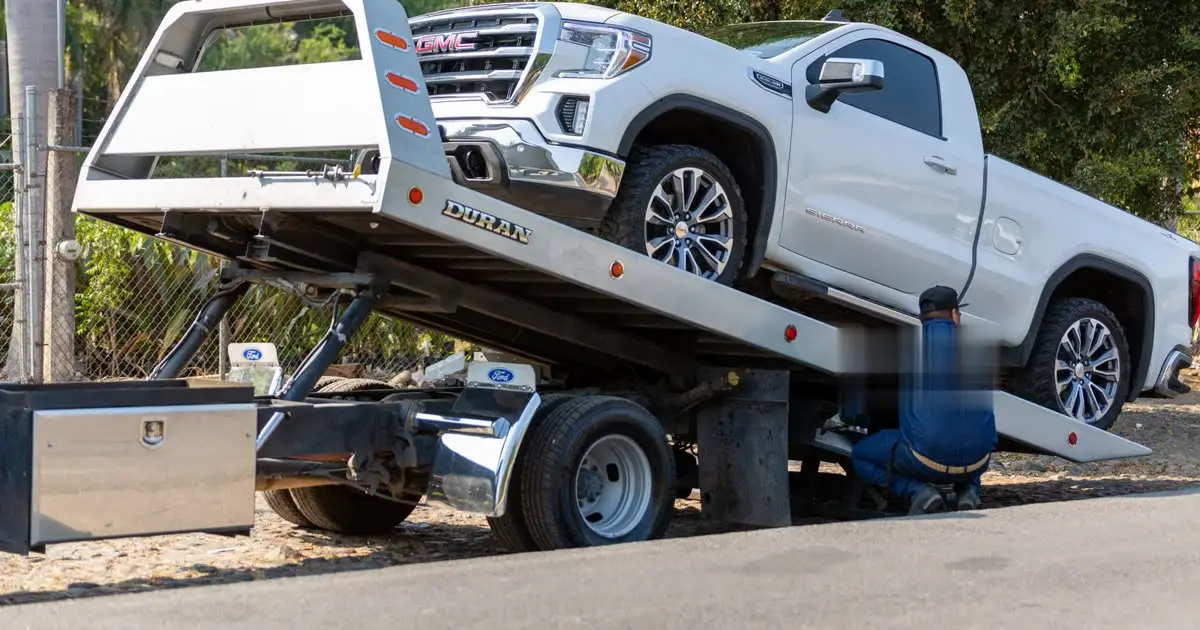 White pickup being loaded onto a rollback tow truck bed
